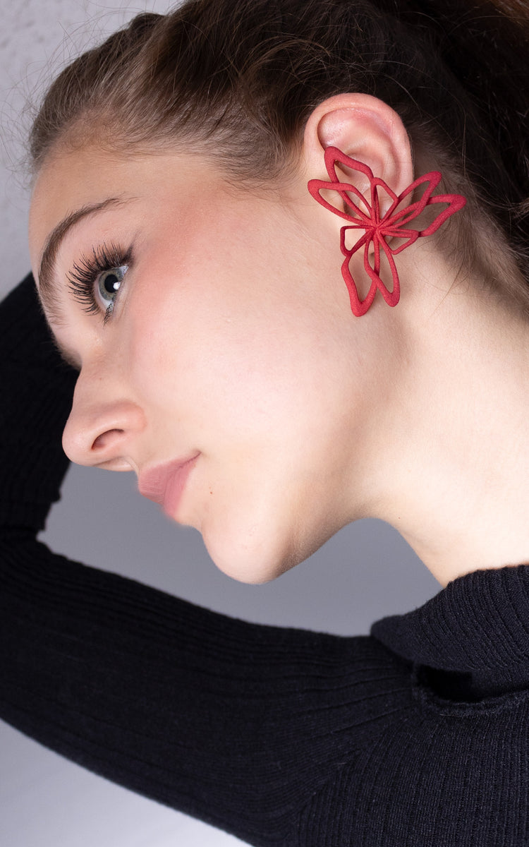 Jeune femme aux cheveux attachés avec jolie bijou rouge florale à l'oreille.