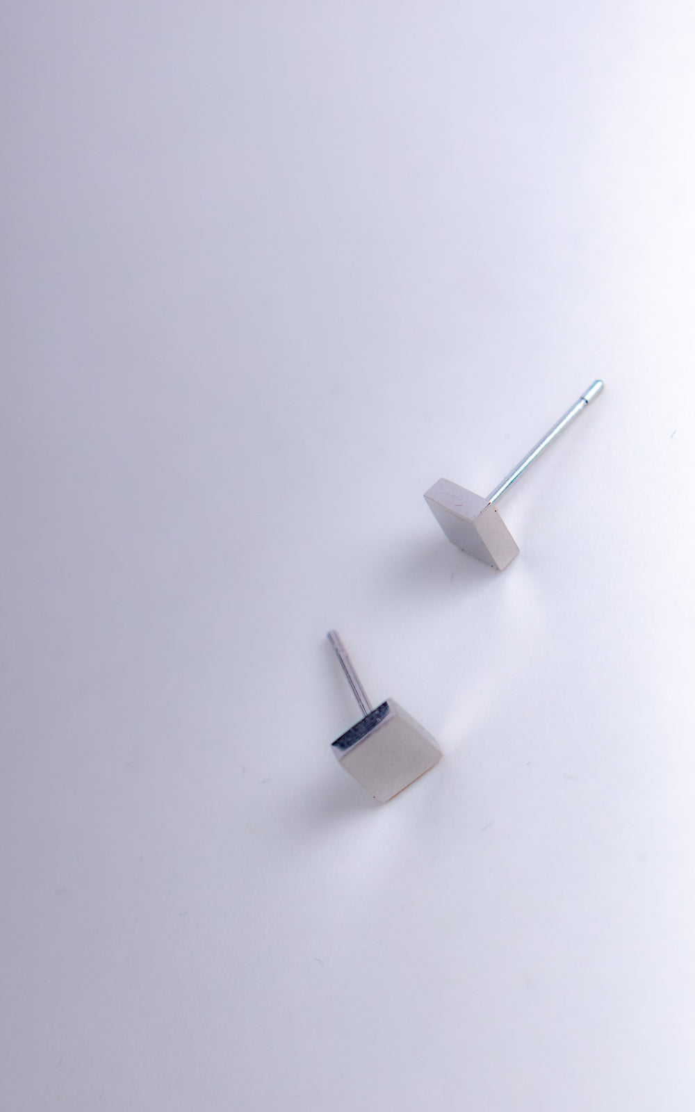 Boucles d’oreilles cube en acier inoxydable argent photographiées en angle, design minimaliste géométrique sur fond clair
