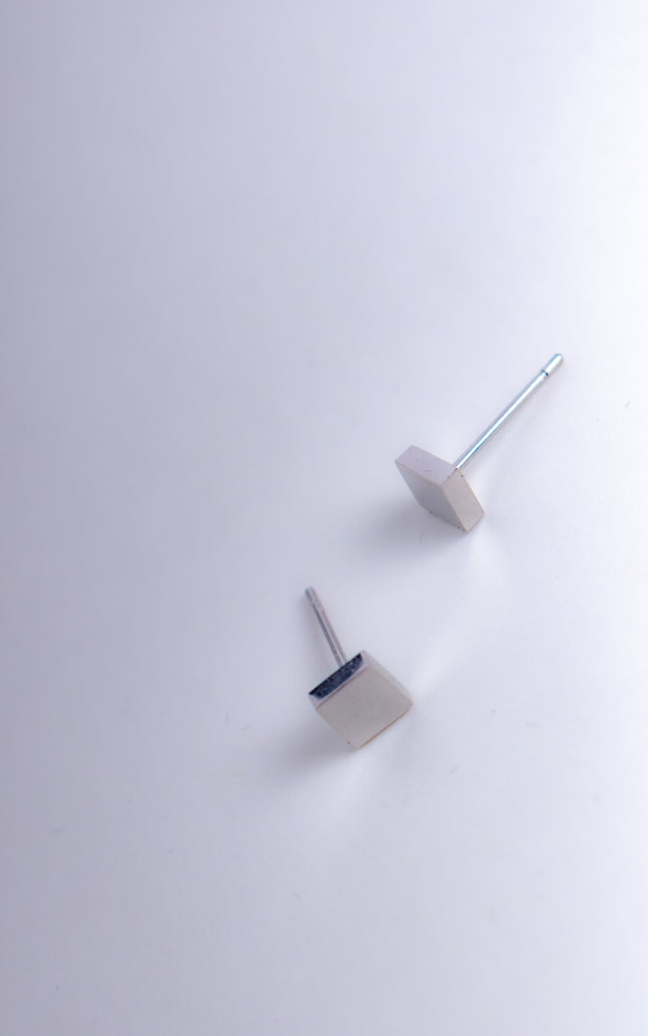Boucles d’oreilles cube en acier inoxydable argent photographiées en angle, design minimaliste géométrique sur fond clair
