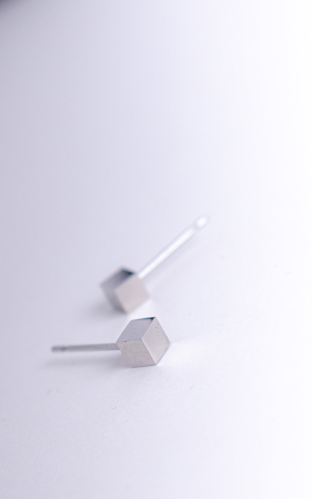Gros plan sur des puces d’oreilles cube en acier inoxydable argent, design minimaliste géométrique avec finition mate