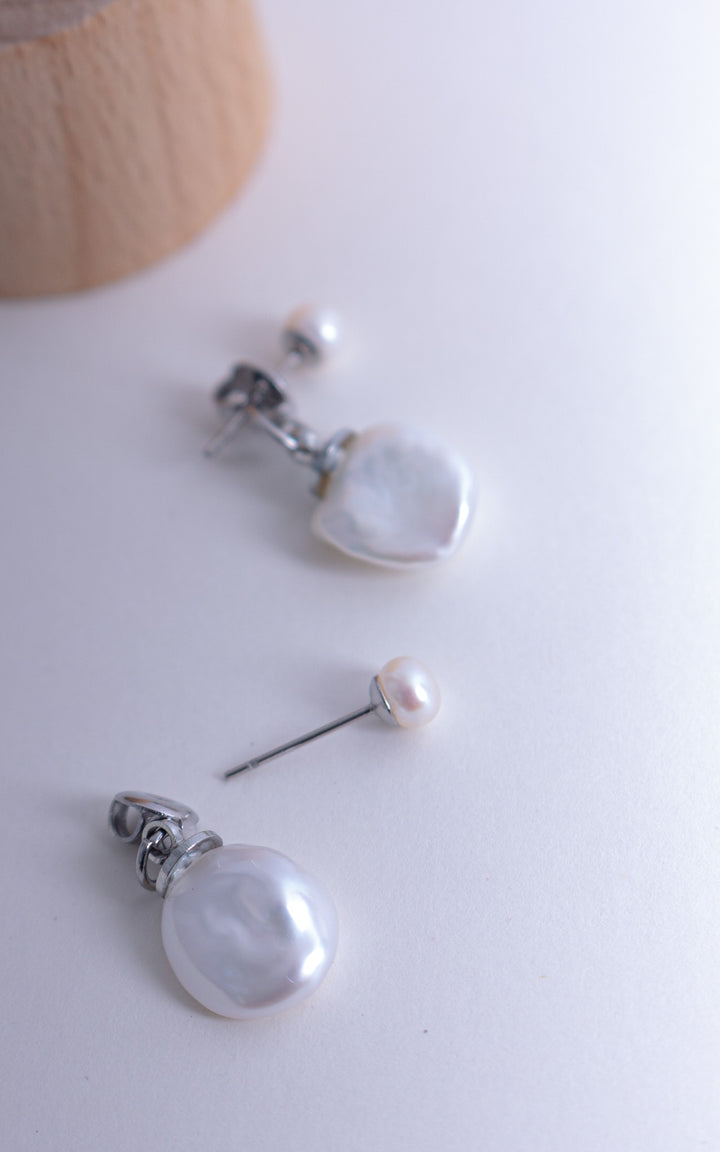 Détail d’une boucle d’oreille veste avec perle baroque suspendue et perle ronde, design élégant et contemporain