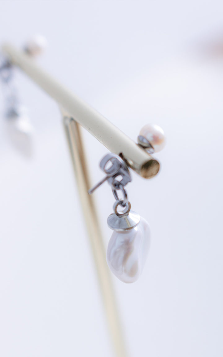 Boucles d’oreilles veste avec perle baroque suspendue et perle ronde arrière, portées sur support, design élégant et contemporain