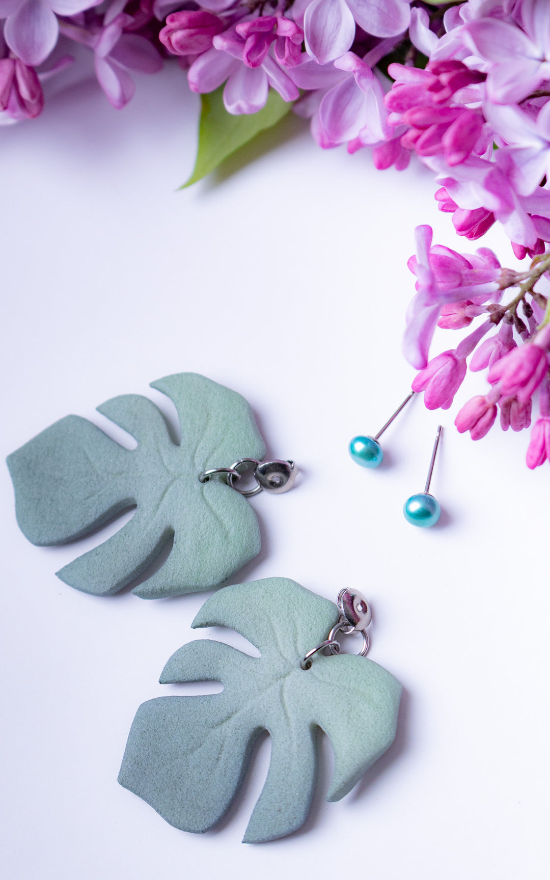 Boucles d’oreilles MAUI Lagoon édition limitée avec feuilles Monstera vert lagon et perles turquoise sur fond floral lilas